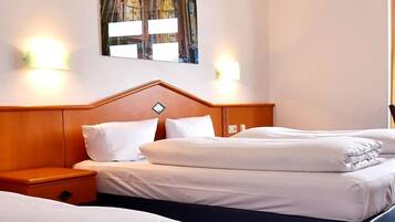 Quarto de hotel com duas camas, uma cabeceira de madeira e um quadro de um edifício na parede.