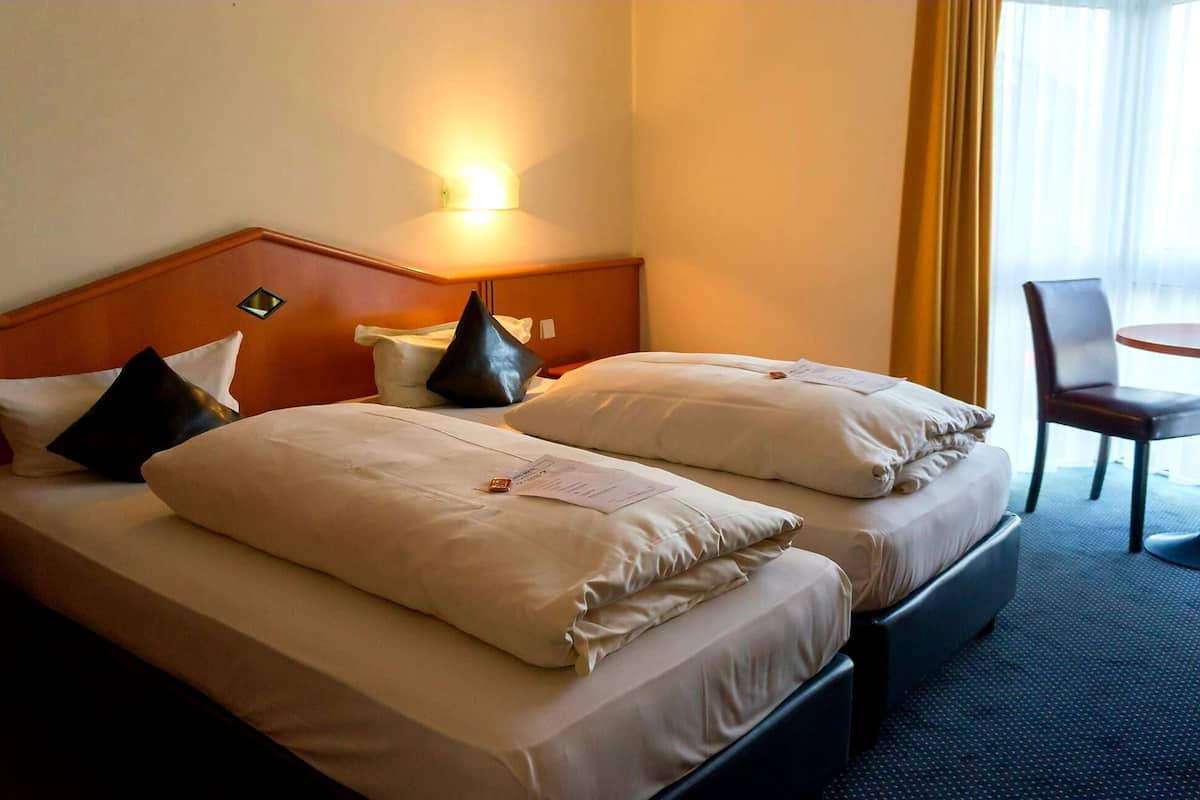 A hotel room with two beds, a nightstand, a chair, and a window with curtains.
