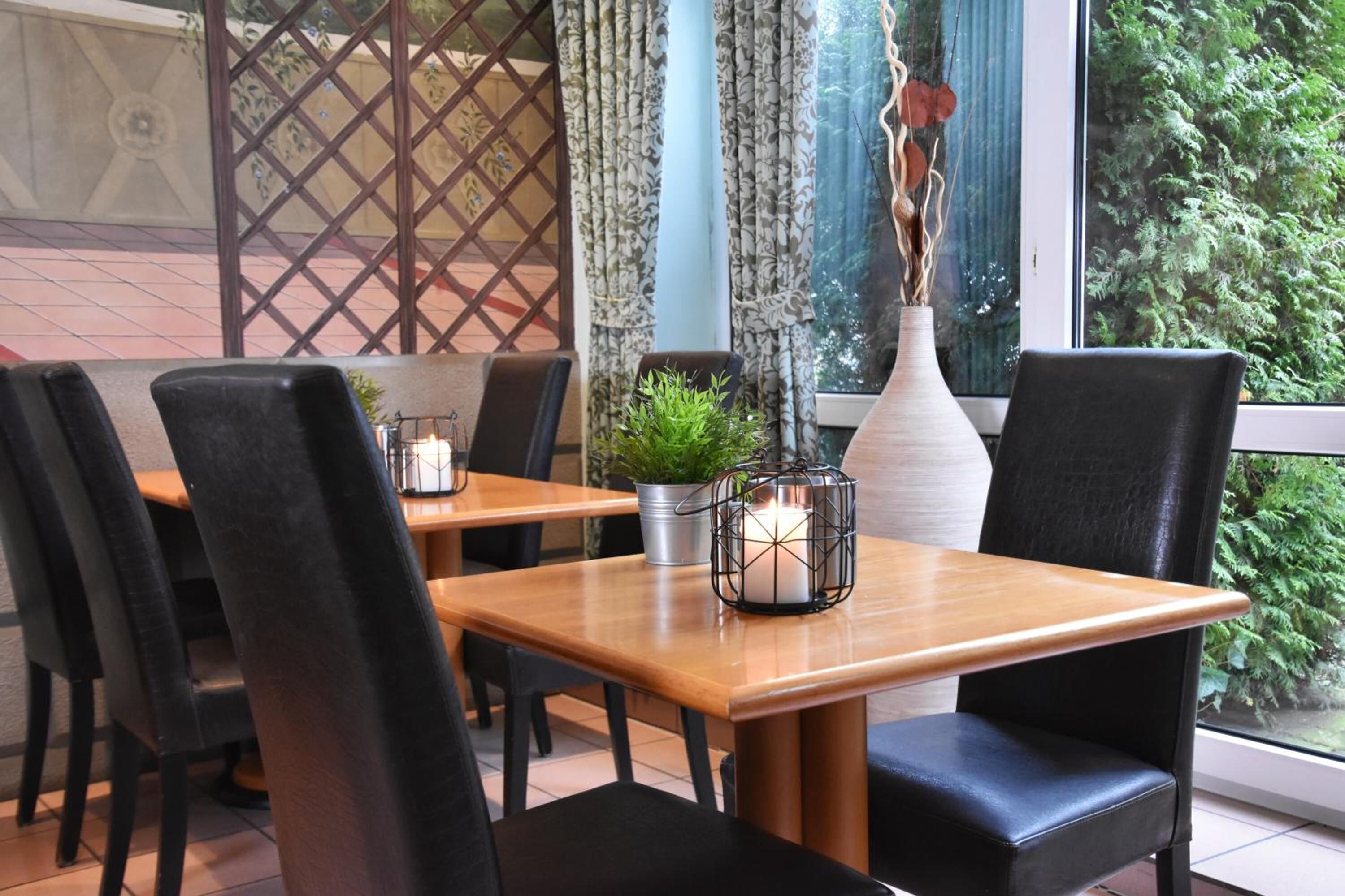 A dining area with wooden tables and black chairs, a potted plant, and a candle on one table.