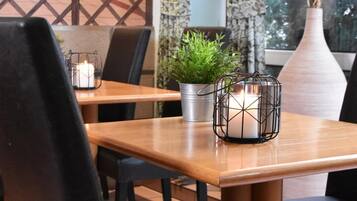 Un comedor con una mesa de madera, sillas negras, una vela en un candelabro, una planta en maceta y un florero con planta.