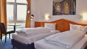 Una habitación de hotel con dos camas, una silla, una mesita y un cuadro en la pared.