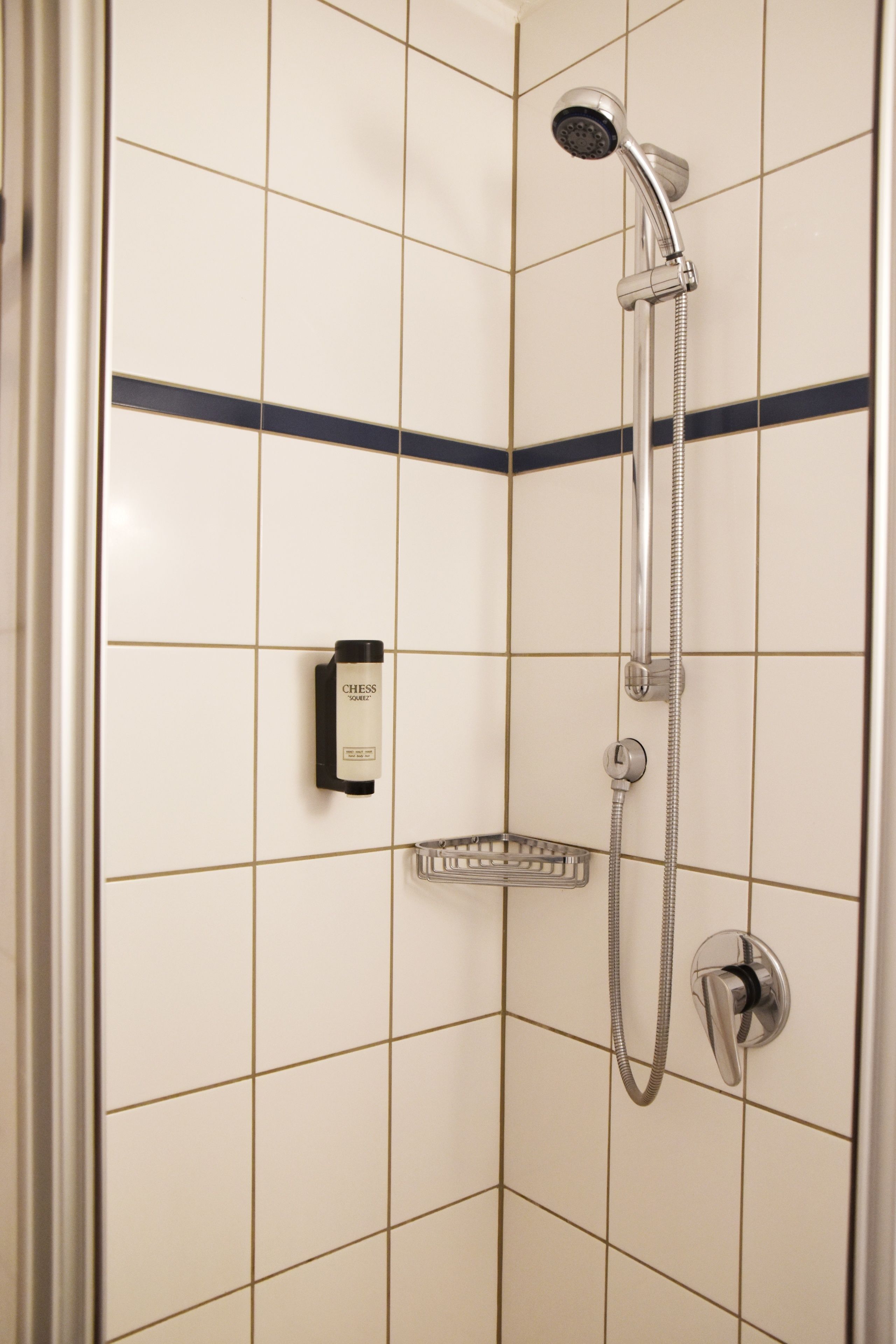En duschhörna med ett duschmunstycke som kan hållas i handen, en väggmonterad tvåldispenser och ett hörnsköljfat.