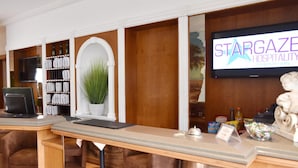 Un área de recepción con mostrador, una pantalla de televisión mostrando 'Stargaze Hospitality' y una planta en maceta.
