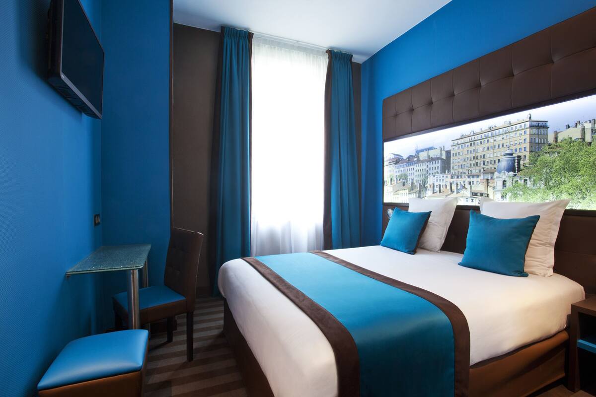 Une chambre d’hôtel avec un grand lit, un bureau et une chaise. Il y a une fenêtre donnant sur la ville.