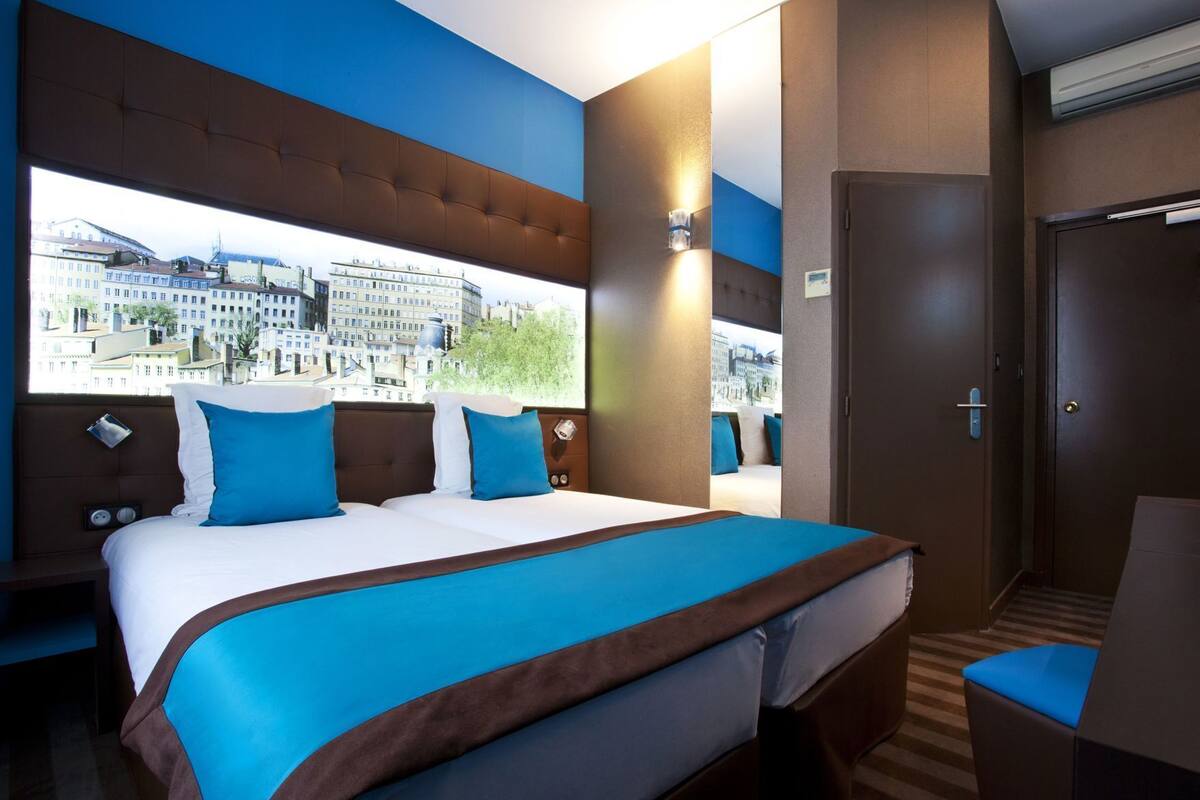 Une chambre d’hôtel avec un grand lit, une vue sur les immeubles, une porte et une table de chevet.