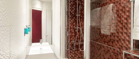 A modern bathroom with a white sink, a glass shower enclosure, and a red-tiled shower area.