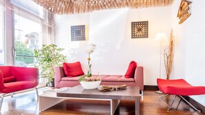 Una sala de estar moderna con un sofá, dos sillones rojos, una mesa de centro y una orquídea en maceta.