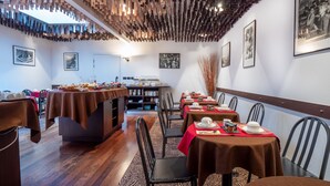 Un comedor con paneles de techo de madera, mesas dispuestas con manteles rojos y cuadros en las paredes.