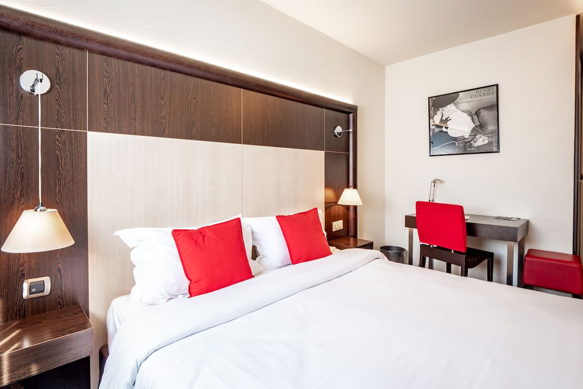 A hotel room with a large bed, a desk with a chair, and a painting on the wall.