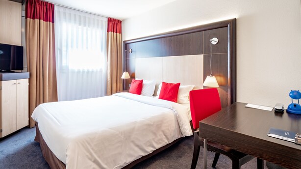 A hotel room with a large bed, a desk, a chair, a television, and a lamp. - Hôtel de Bonlieu (Annecy)
