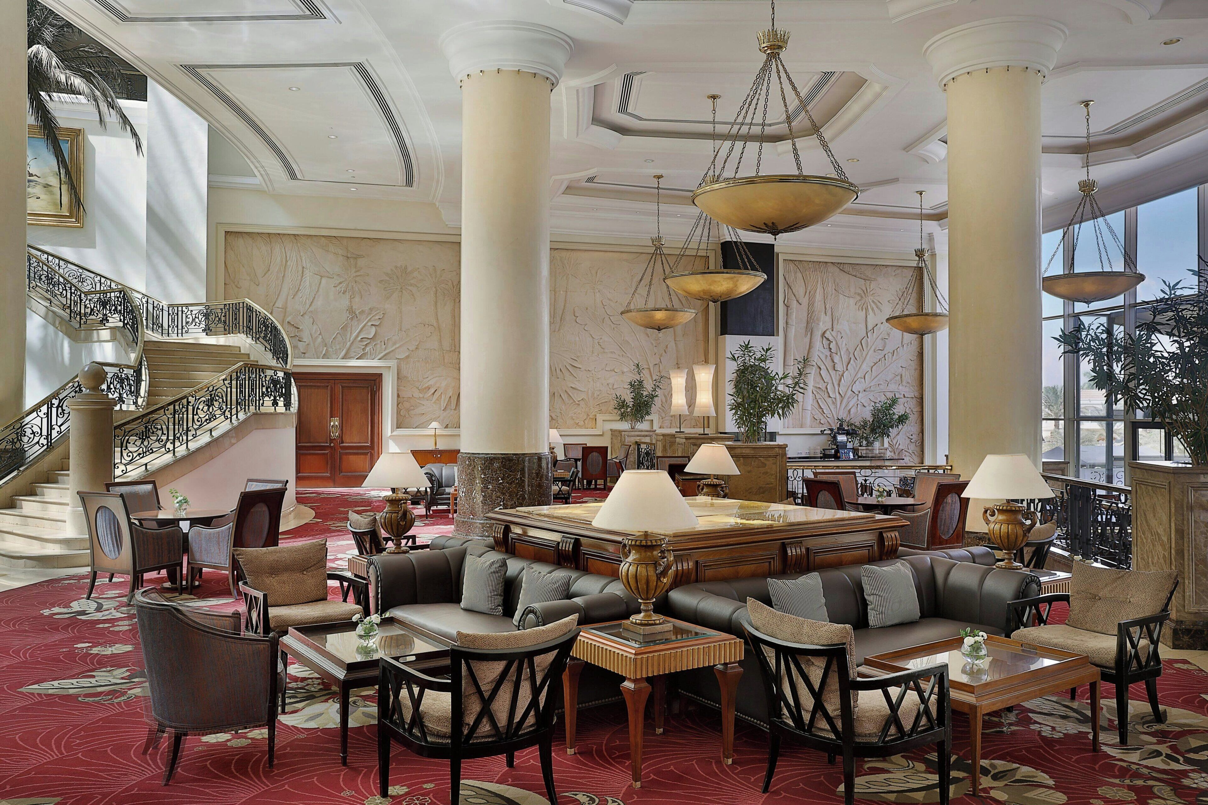 A spacious lobby with a grand staircase, multiple seating areas, and large chandeliers.