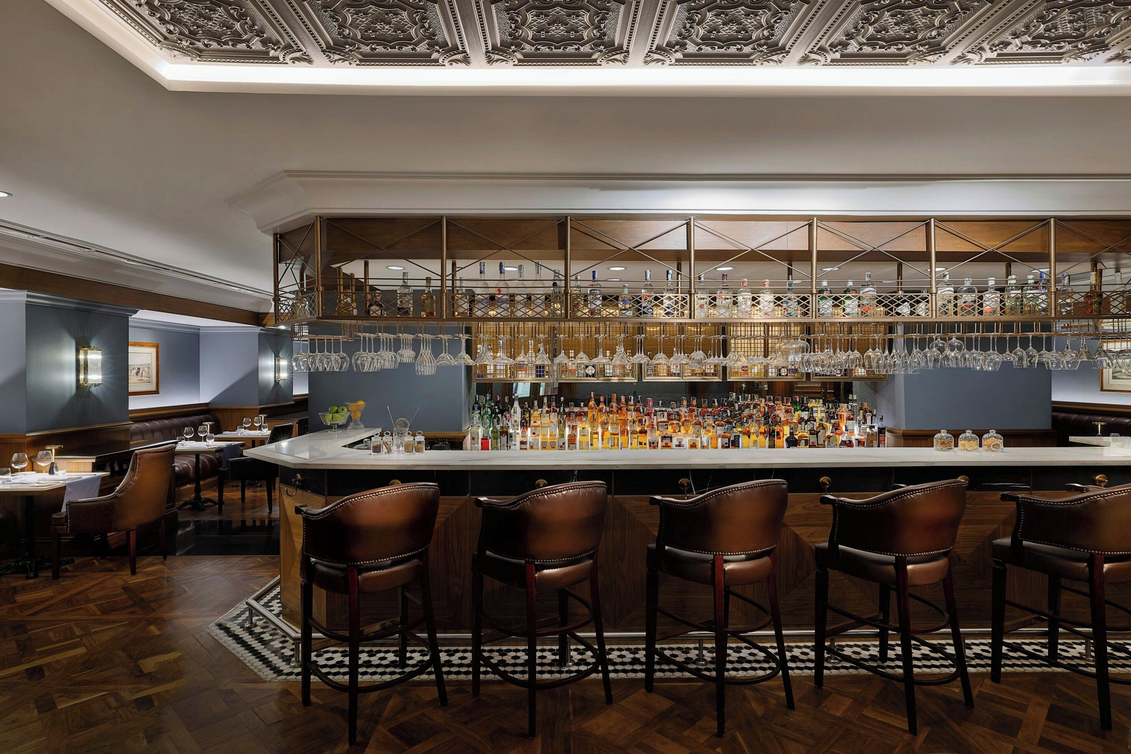 Zona de bar con mostrador alto, diversas opciones de asientos y una variedad de botellas y vasos.