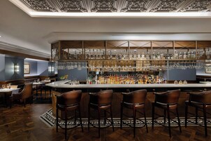 Zona de bar con mostrador alto, diversas opciones de asientos y una variedad de botellas y vasos.