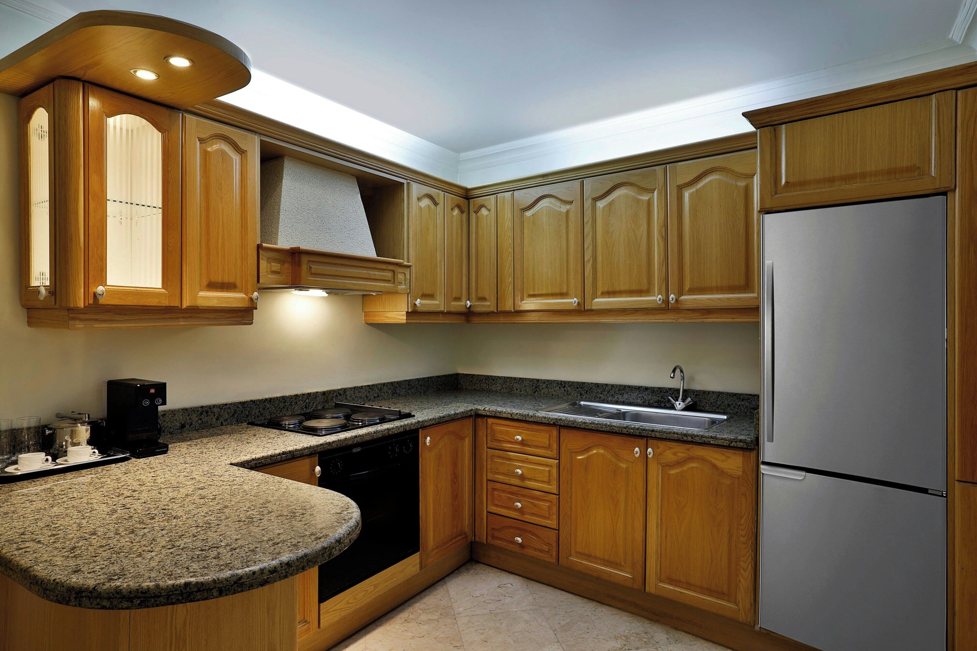 A kitchen with wooden cabinets, a stainless steel refrigerator, a built-in oven, and a granite countertop.