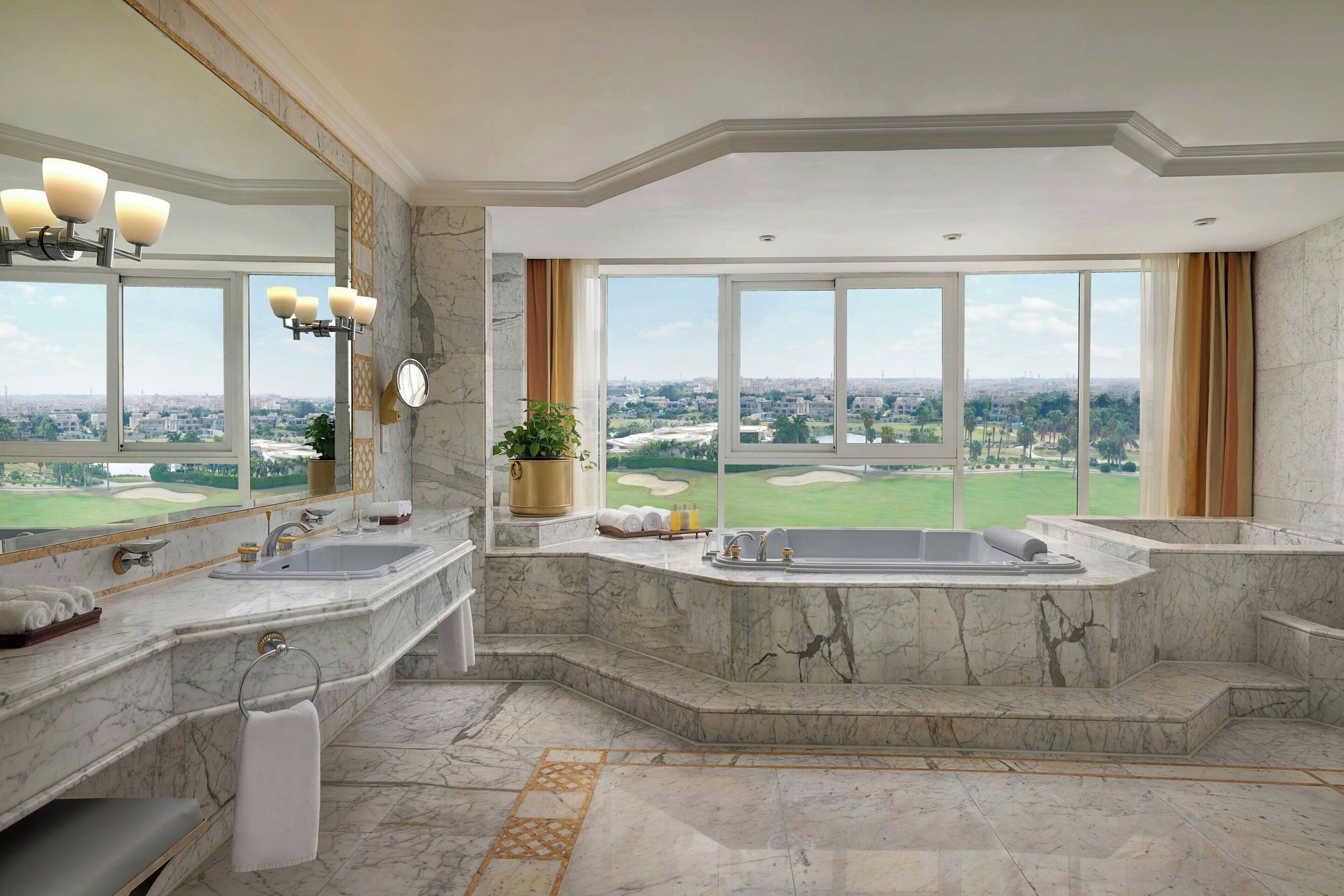Un baño lujoso con una bañera grande, lavamanos doble y un espejo amplio. Cuenta con piso de mármol y vistas a un campo de golf.