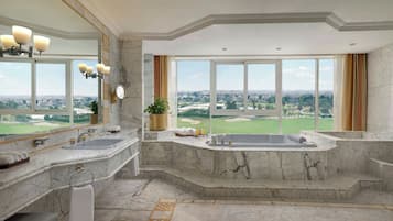 Un baño lujoso con una bañera grande, lavamanos doble y un espejo amplio. Cuenta con piso de mármol y vistas a un campo de golf.
