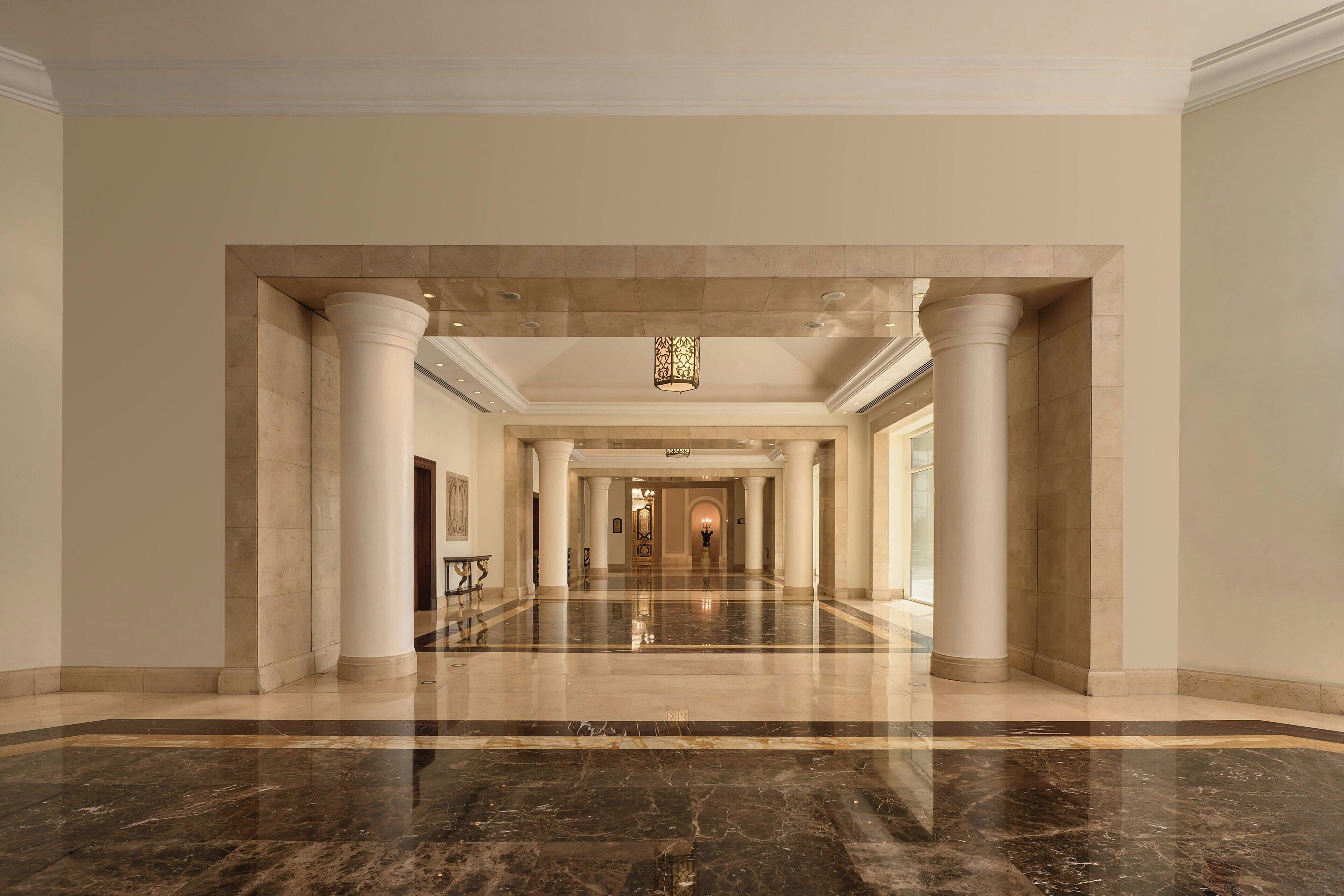 Um hall amplo com piso de mármore, colunas brancas e um lustre central.