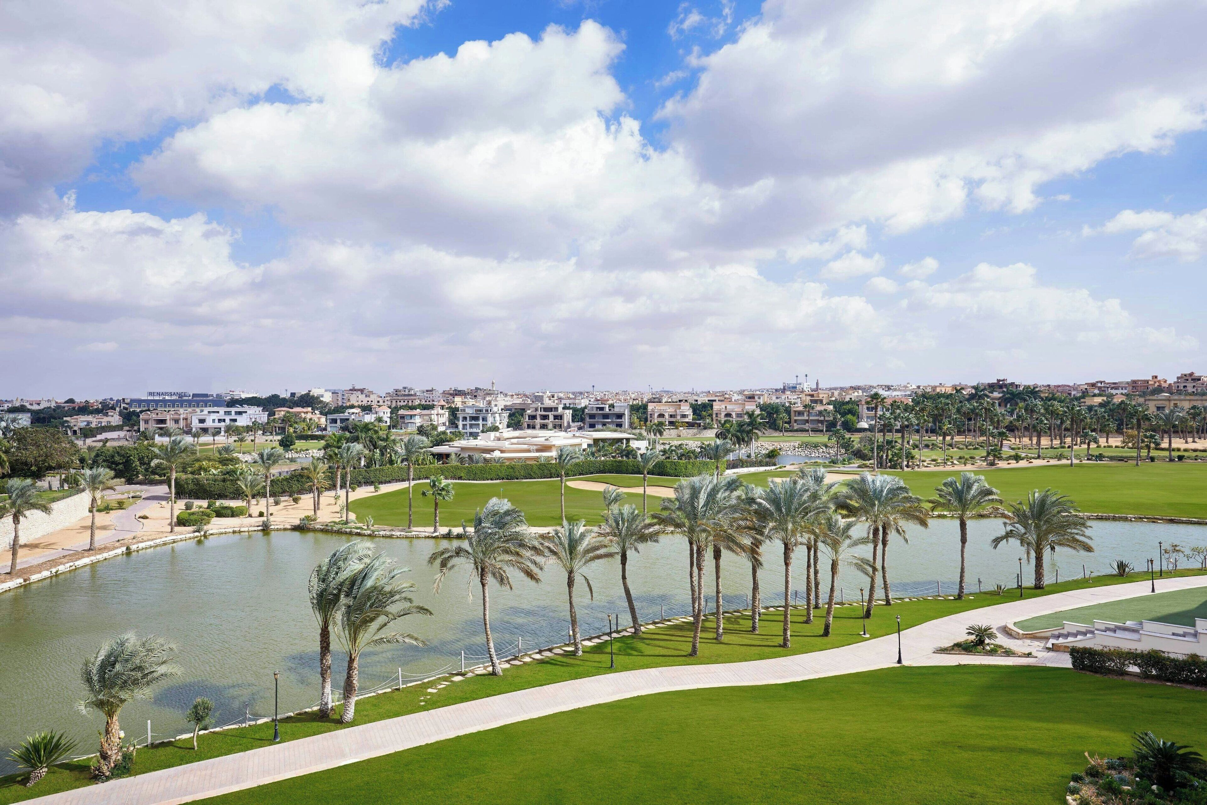 A golf course with a pond, palm trees, and a cityscape in the background.