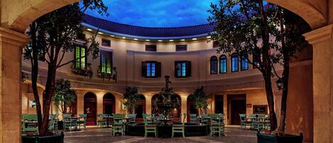 A courtyard with a fountain, seating areas, and a view of the sky through an archway.