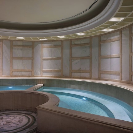 An indoor swimming pool with a curved design, marble walls, and a central column.