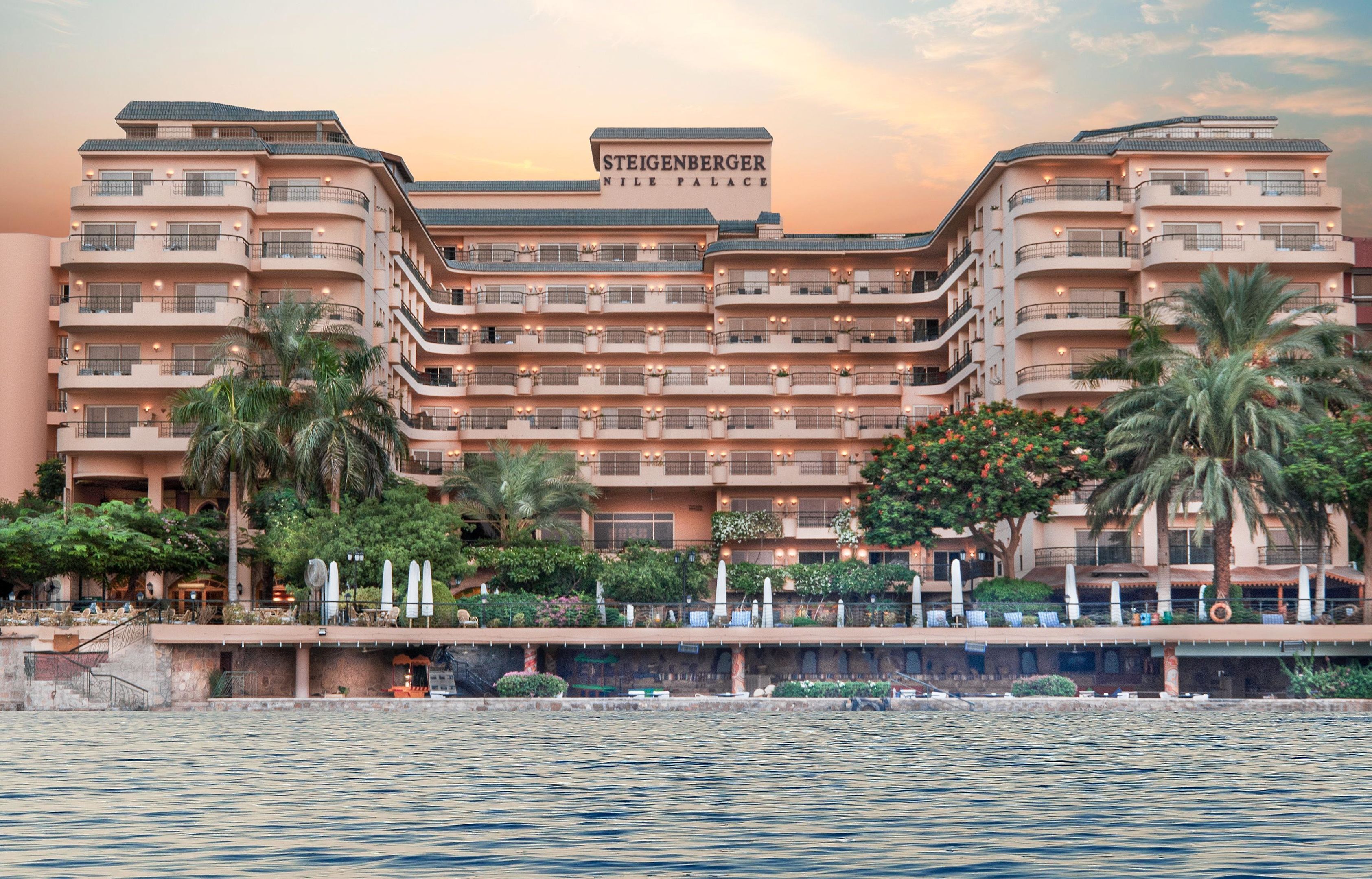 Un hotel de varios pisos con balcones, palmeras y vista al agua.