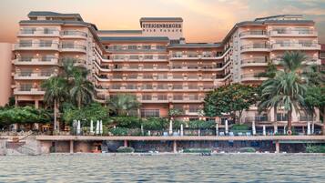 Un hotel de varios pisos con balcones, palmeras y vista al agua.
