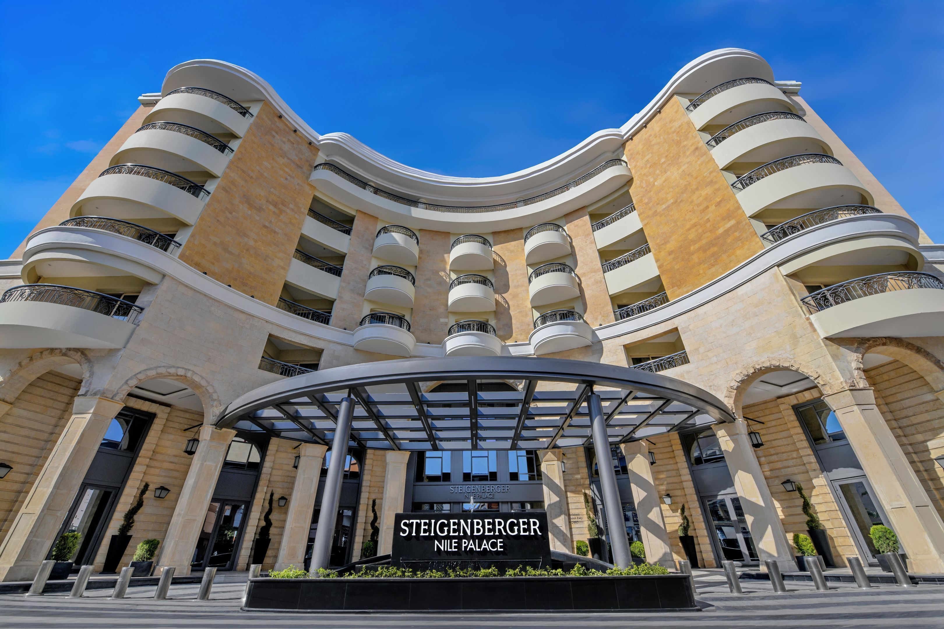 Un hotel de varios pisos con fachada curva, balcones y una entrada central con un cartel que dice "Steigenberger Nile Palace".