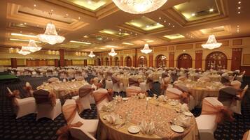 Une salle de banquet avec des tables rondes disposées pour un événement formel, agrémentée de lustres et présentant un style architectural classique.