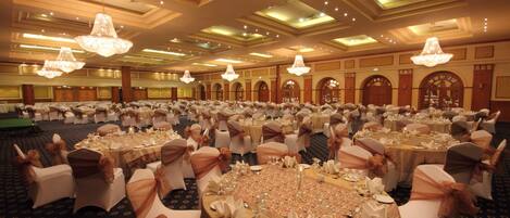 A banquet hall with round tables set for a formal event, featuring chandeliers and a classic architectural design.
