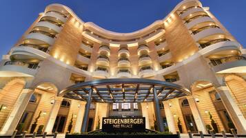 Ein mehrstöckiges Hotel mit geschwungener Fassade, zahlreichen Balkonen und einem zentralen Eingang, der die Beschilderung "Steigenberger Nile Palace" trägt.