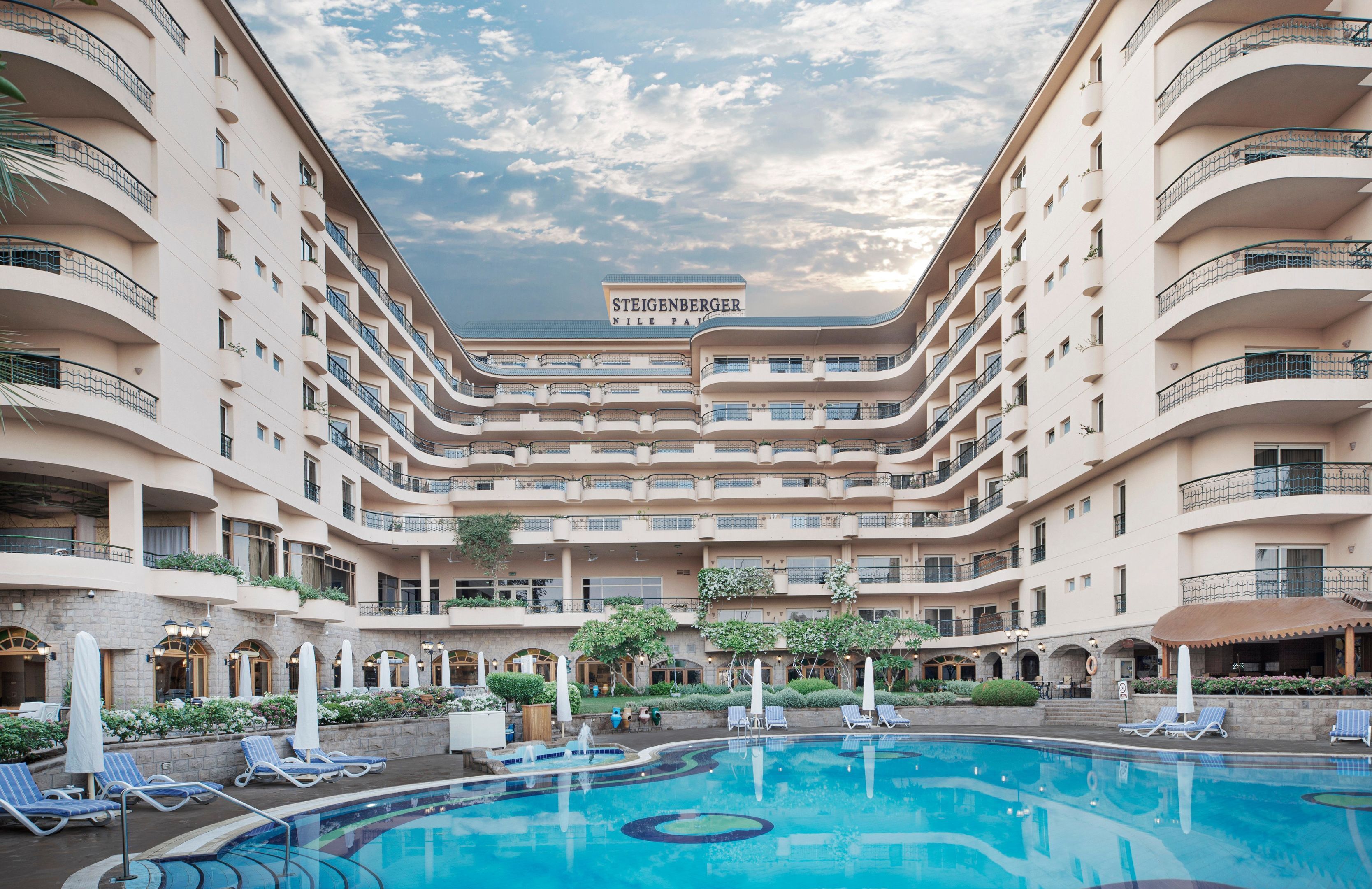 A multi-story hotel with a swimming pool, outdoor seating, and a sign reading "Steigenberger Nile Park".