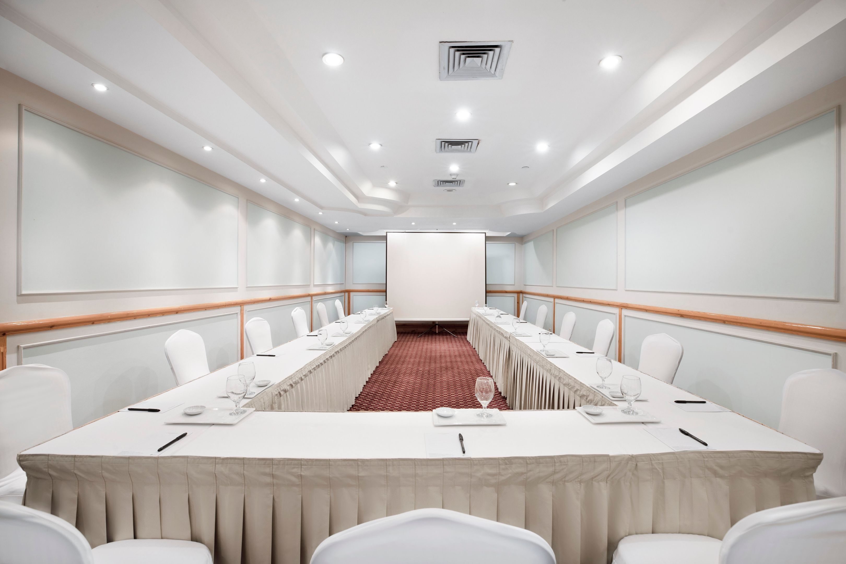 A conference room with a long table, white chairs, and a red carpet.