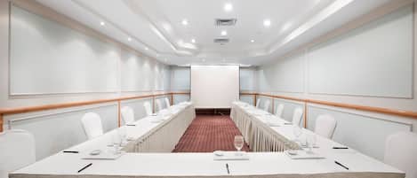 A conference room with a long table, white chairs, and a red carpet.