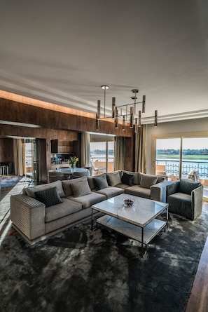 A modern living room with a sectional sofa, a glass coffee table, and a view of a body of water through large windows. - Steigenberger Nile Palace (Luxor)