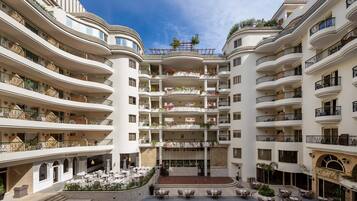 Un hotel de varios pisos con balcones, un patio central con mobiliario de exterior y una zona de bar.