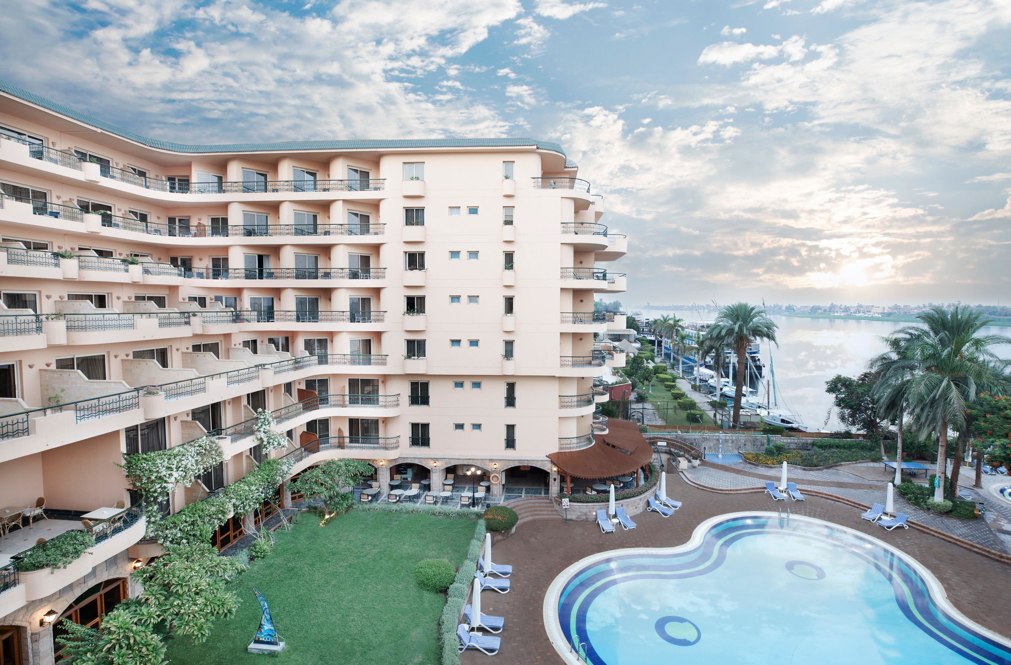 A multi-story hotel with a swimming pool, outdoor seating, and a view of the sea.