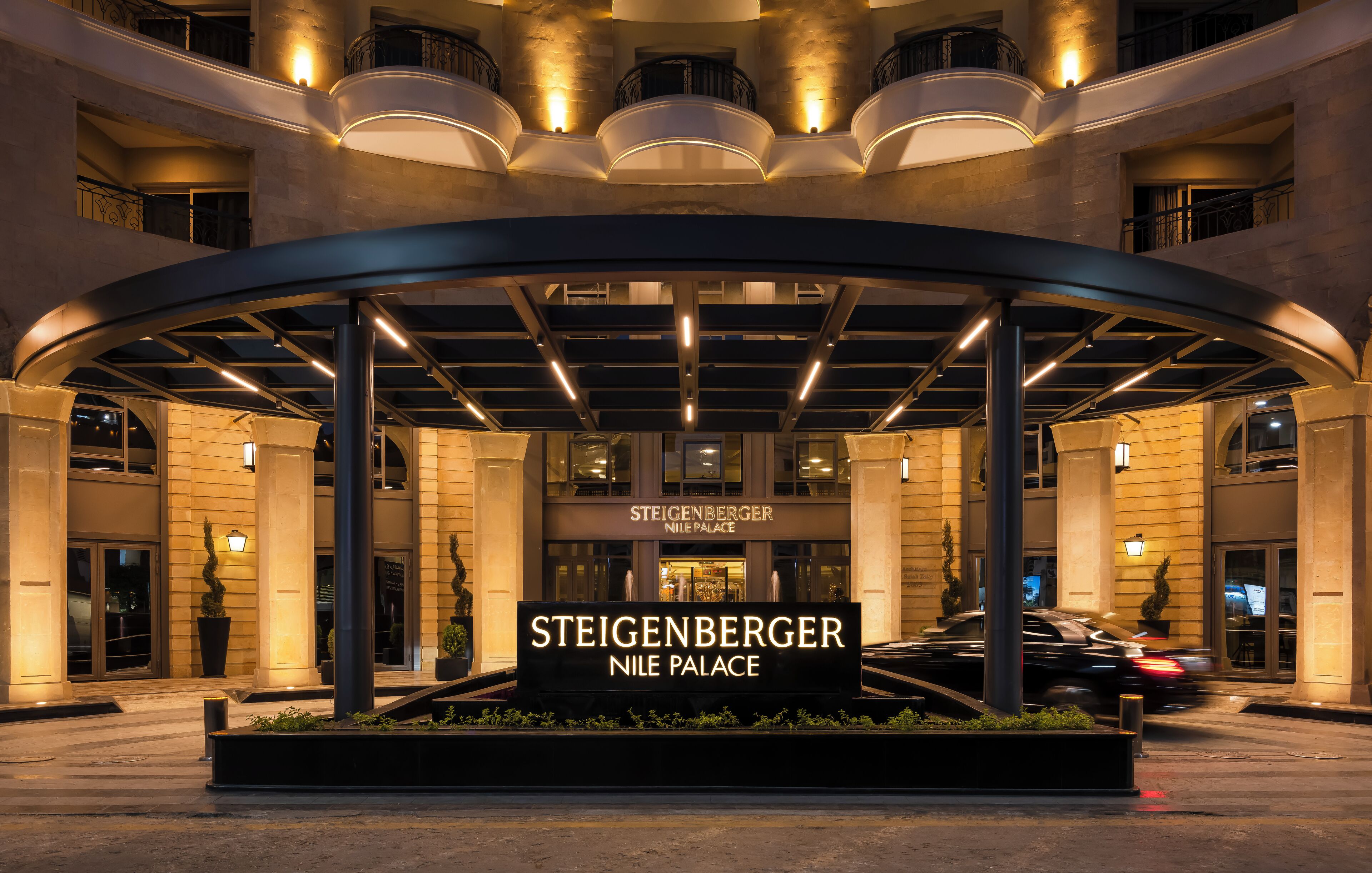 Der Eingang des Steigenberger Nile Palace mit einer gewölbten Markise, beleuchteten Schildern und einer angelegten Grünfläche.