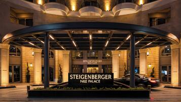 Der Eingang des Steigenberger Nile Palace mit einer gewölbten Markise, beleuchteten Schildern und einer angelegten Grünfläche.