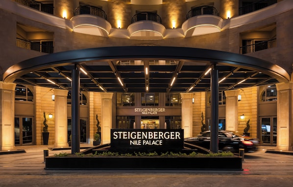 The entrance of Steigenberger Nile Palace with a curved canopy, illuminated signs, and a landscaped area.