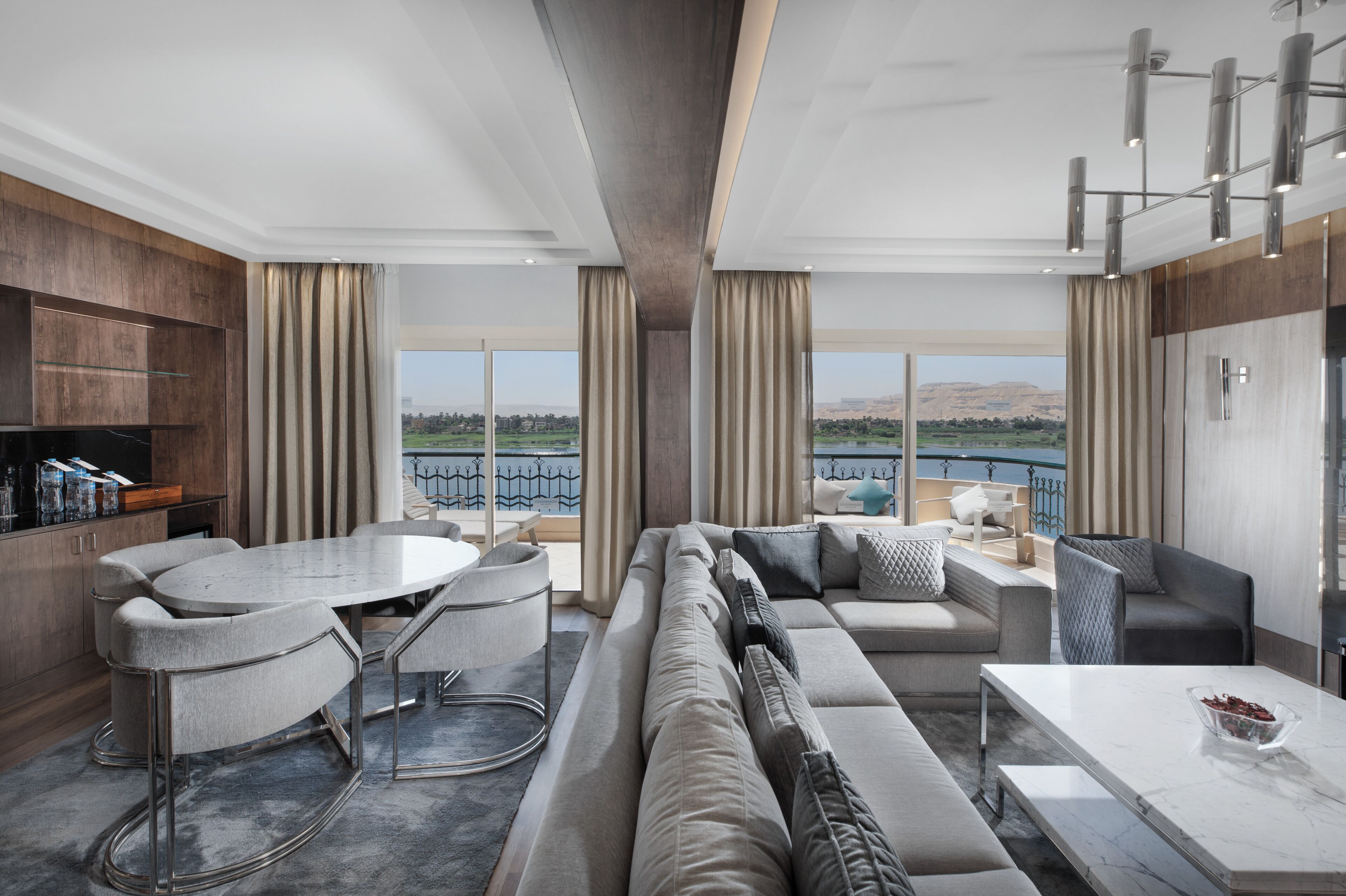 A modern living room with a large sofa, a dining table, and a view of a body of water.
