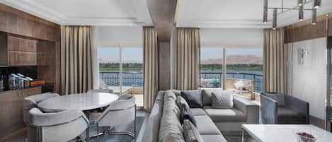 A modern living room with a large sofa, a dining table, and a view of a body of water.