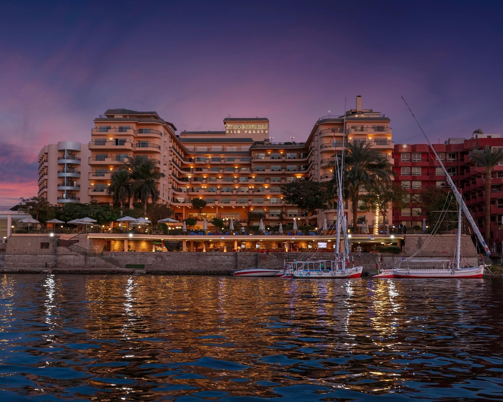 Un hotel con múltiples balcones, vista al agua y un velero amarrado cerca.