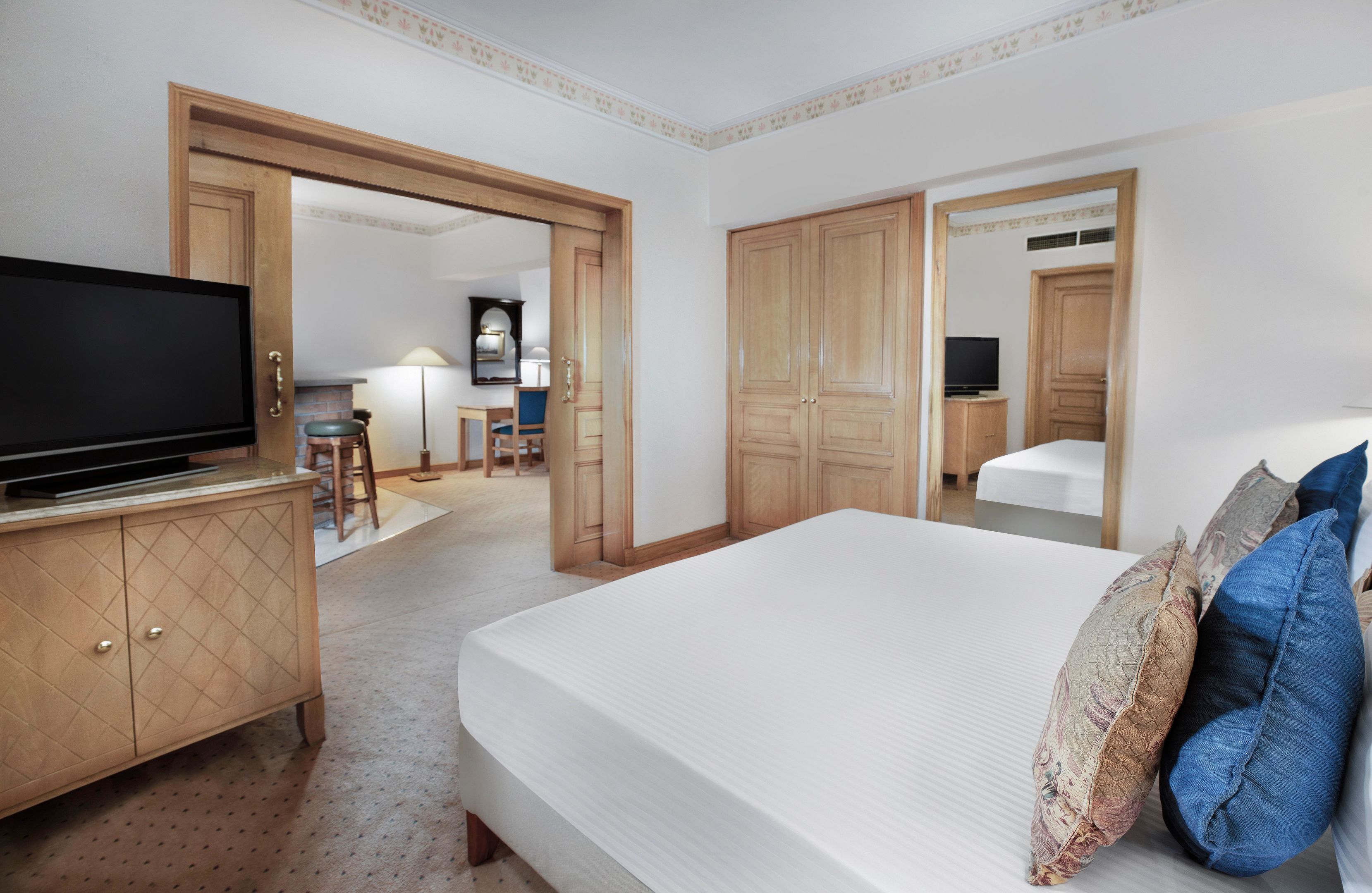 A hotel room with a bed, a TV on a wooden cabinet, a desk with a chair, and a wardrobe.