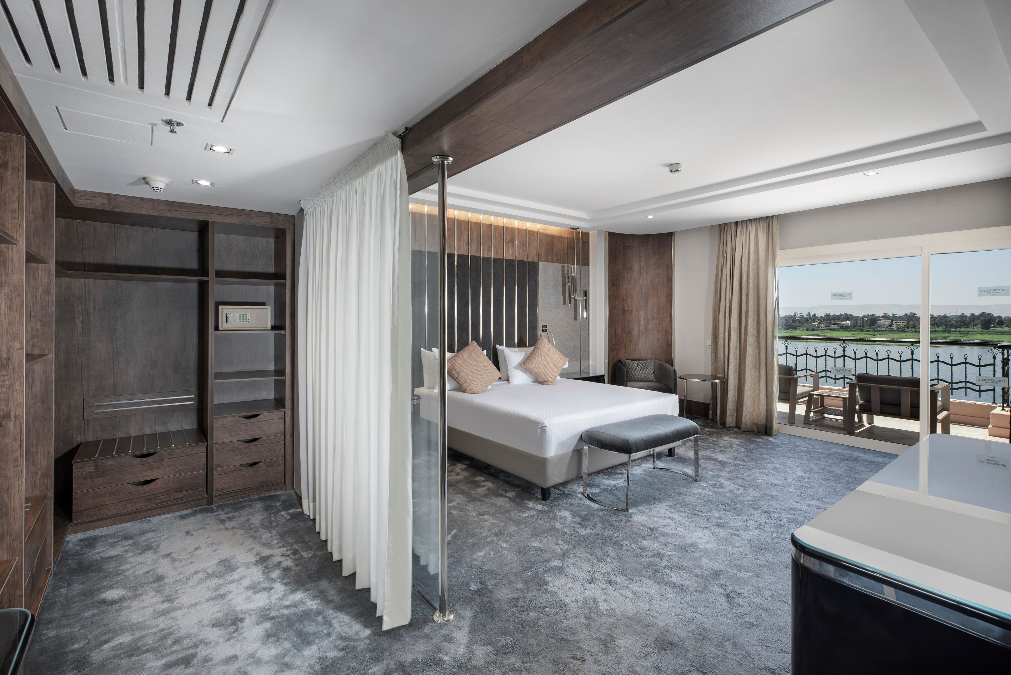 A modern hotel room with a large bed, a walk-in closet, a balcony with a view, and a dining area.