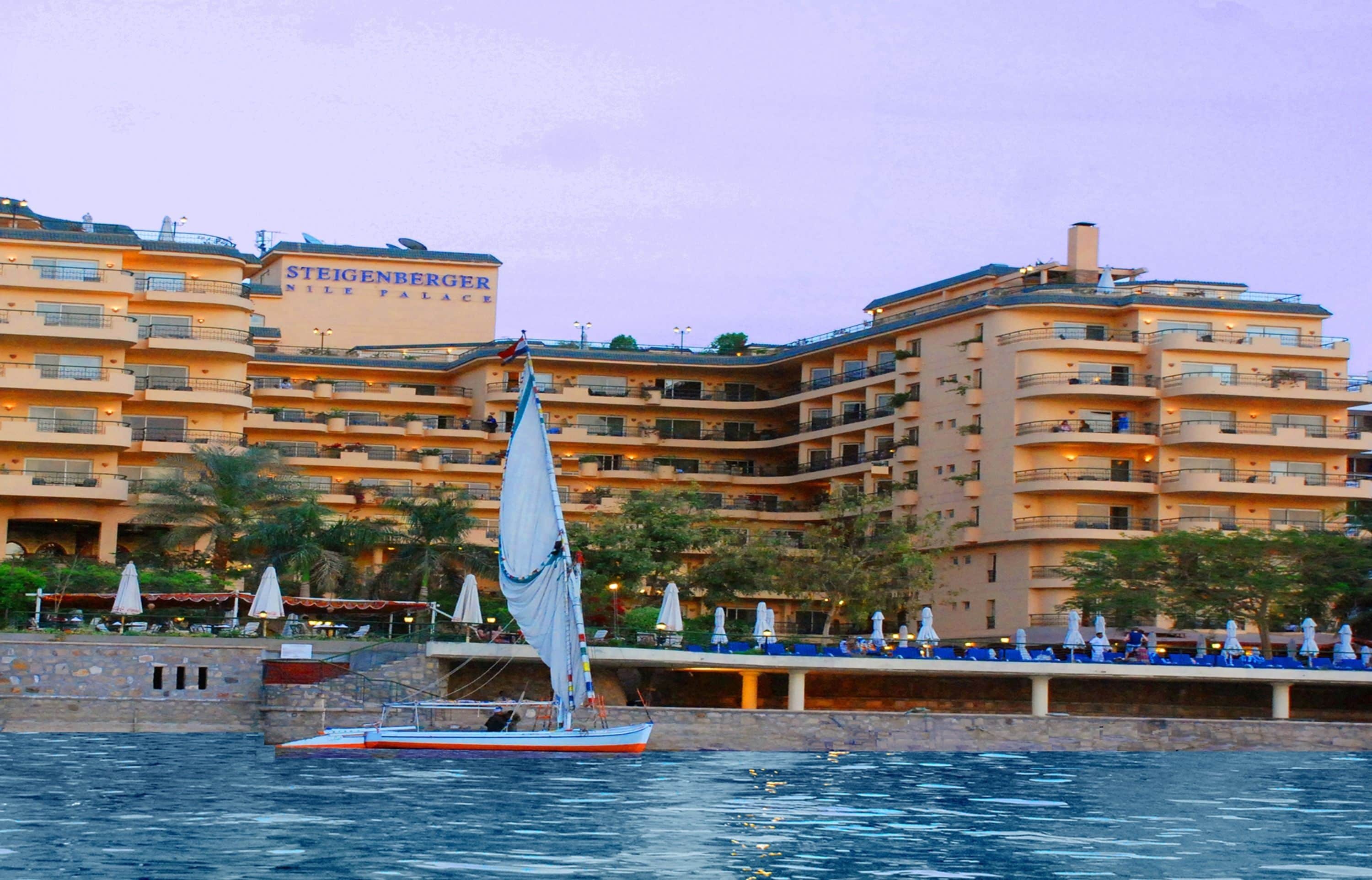 A waterfront hotel with a sailboat, balconies, and outdoor seating.