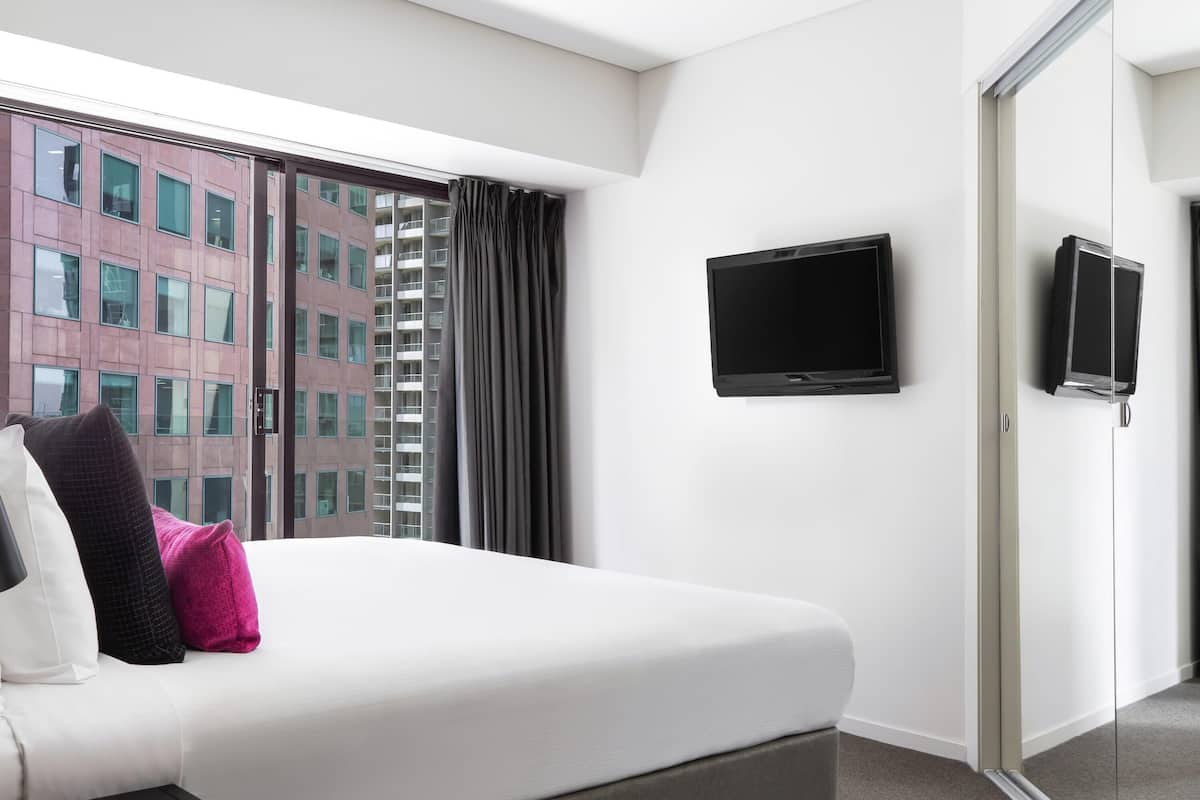 A hotel room with a bed, a TV, a sliding door, and a view of a building.