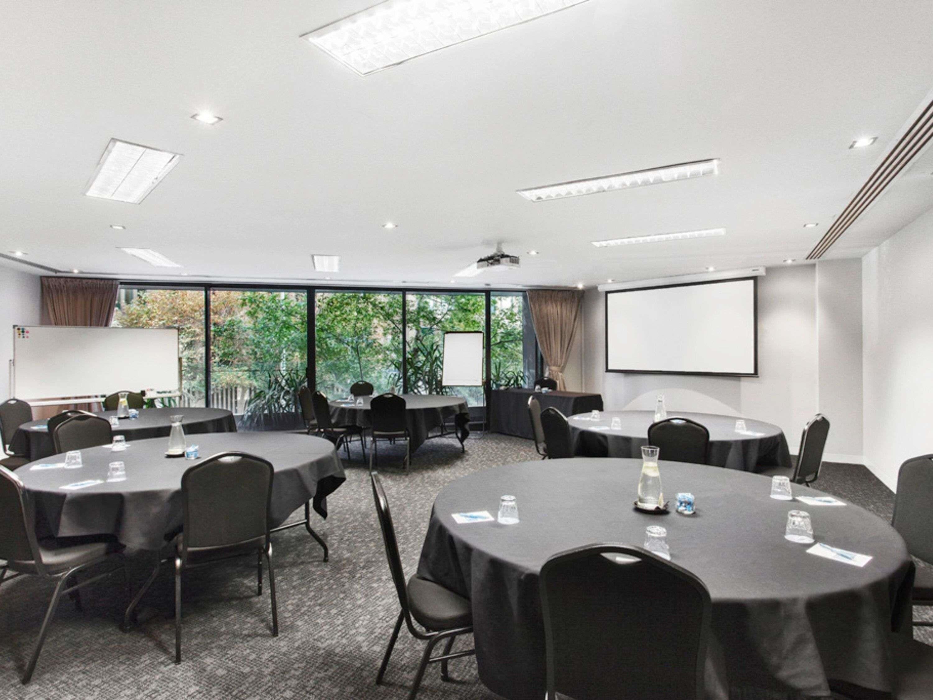 A conference room with round tables, chairs, a projector screen, and a whiteboard.