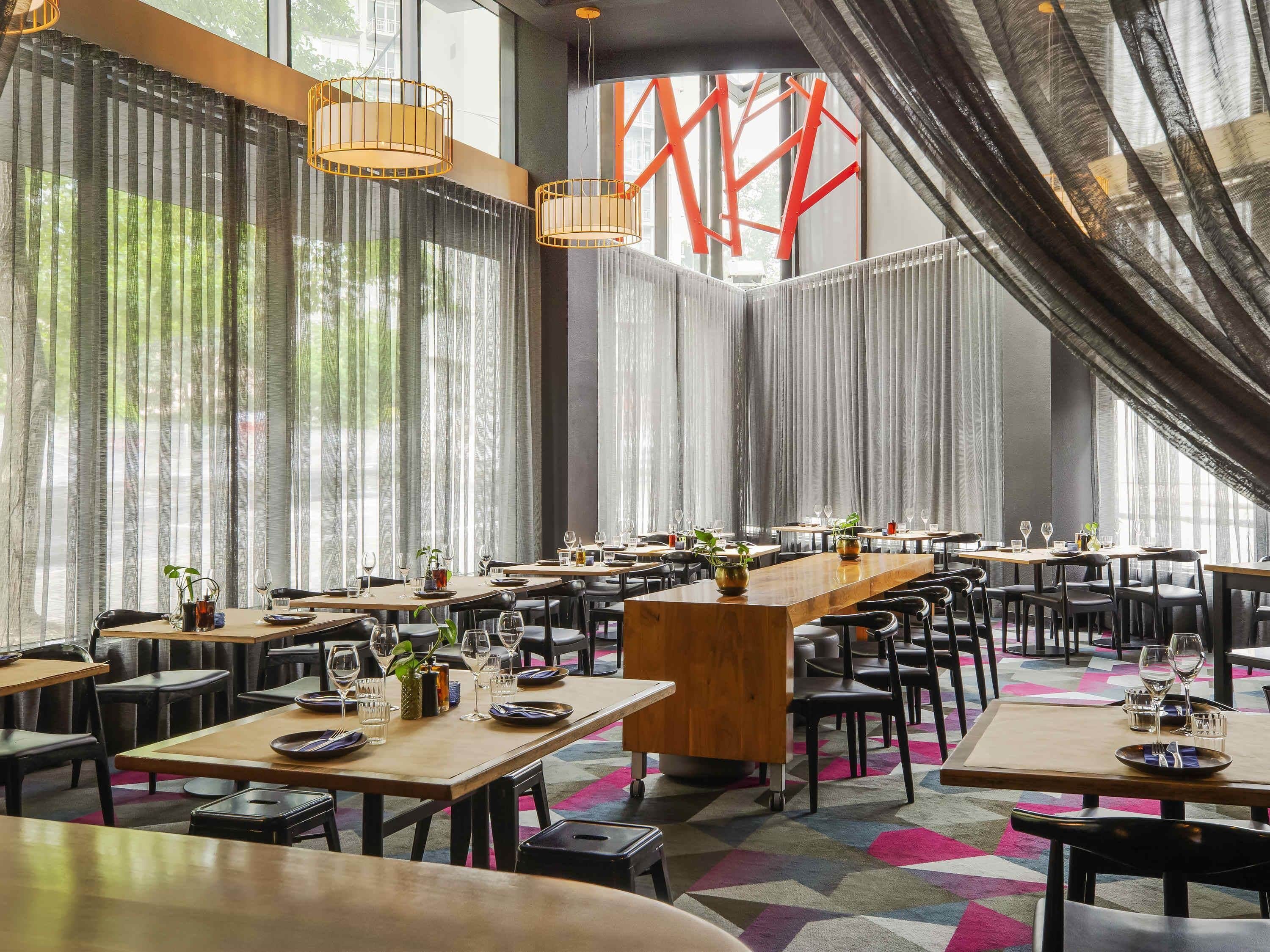Ein Restaurant mit mehreren Tischen, Stühlen und hängenden Pendelleuchten.