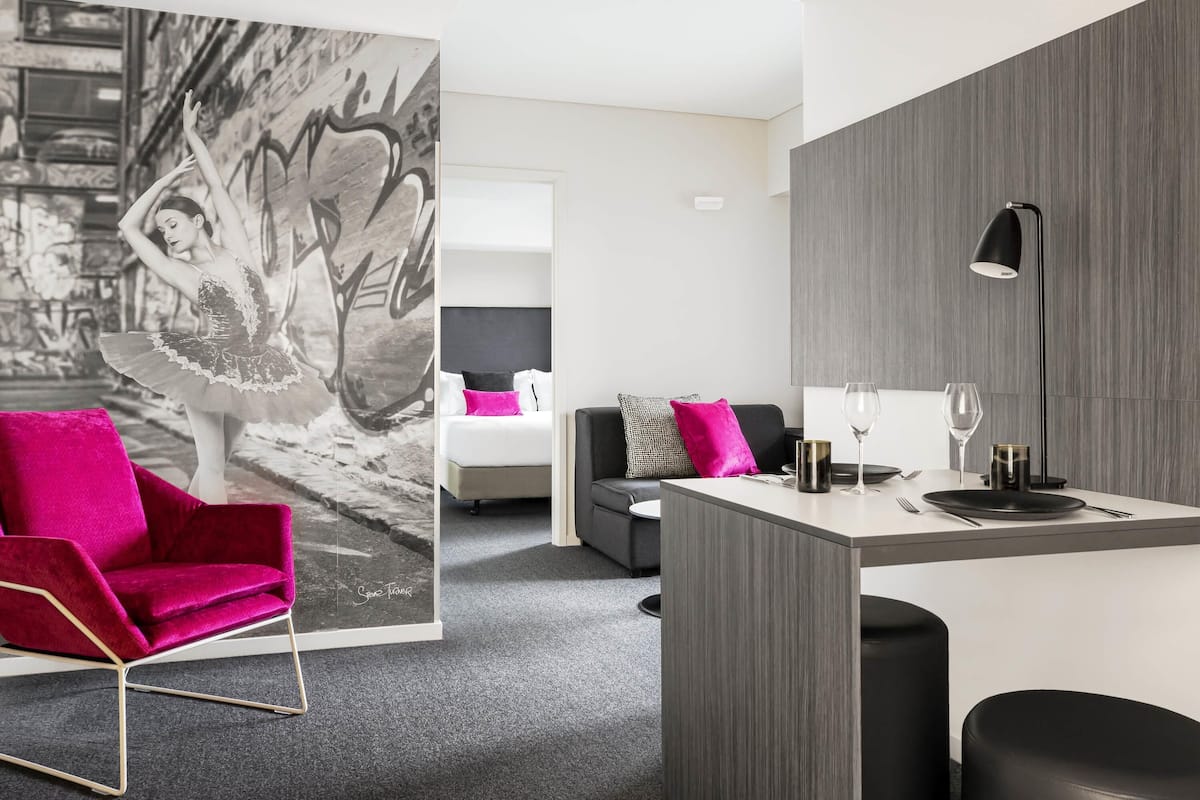 A modern room with a red chair, a grey sofa, a small table with a lamp, and a wall with a black and white photo.