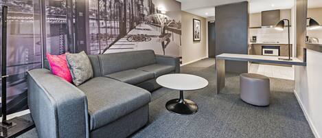 A modern hotel room with a grey sofa, a round table, and a large cityscape mural on the wall.